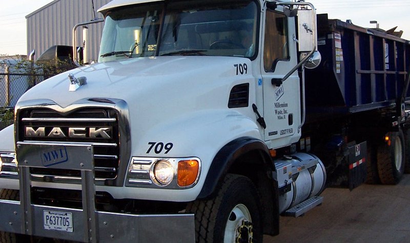 Photo of a Millennium Waste truck collecting a full roll-off waste bin.